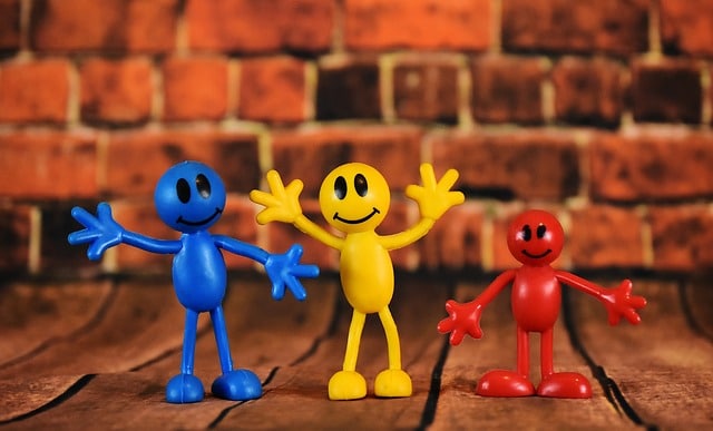 Drei bunte Spielfiguren mit erhobenen Armen vor einer Backsteinwand