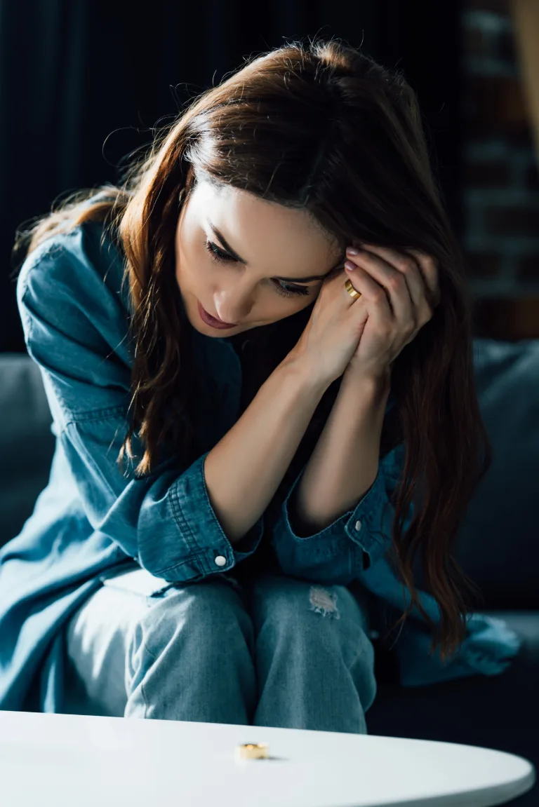 Hochsensible Frau sitzt abends erschöpft auf dem Sofa, die Hände am Gesicht