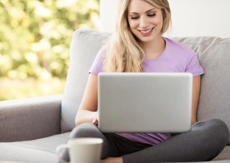 Lächelnde Frau sitzt mit Laptop auf dem Sofa und informiert sich über eine Ausbildung