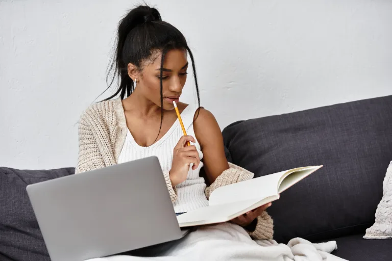 Junge Frau lernt zu Hause mit Buch und Laptop
