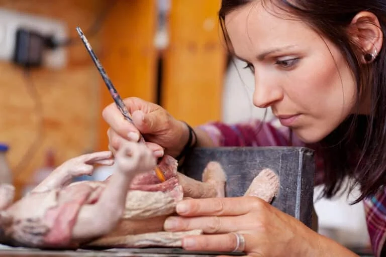 Junge Frau bemalt mit einem feinen Pinsel konzentriert eine kleine Figur in einer Werkstatt