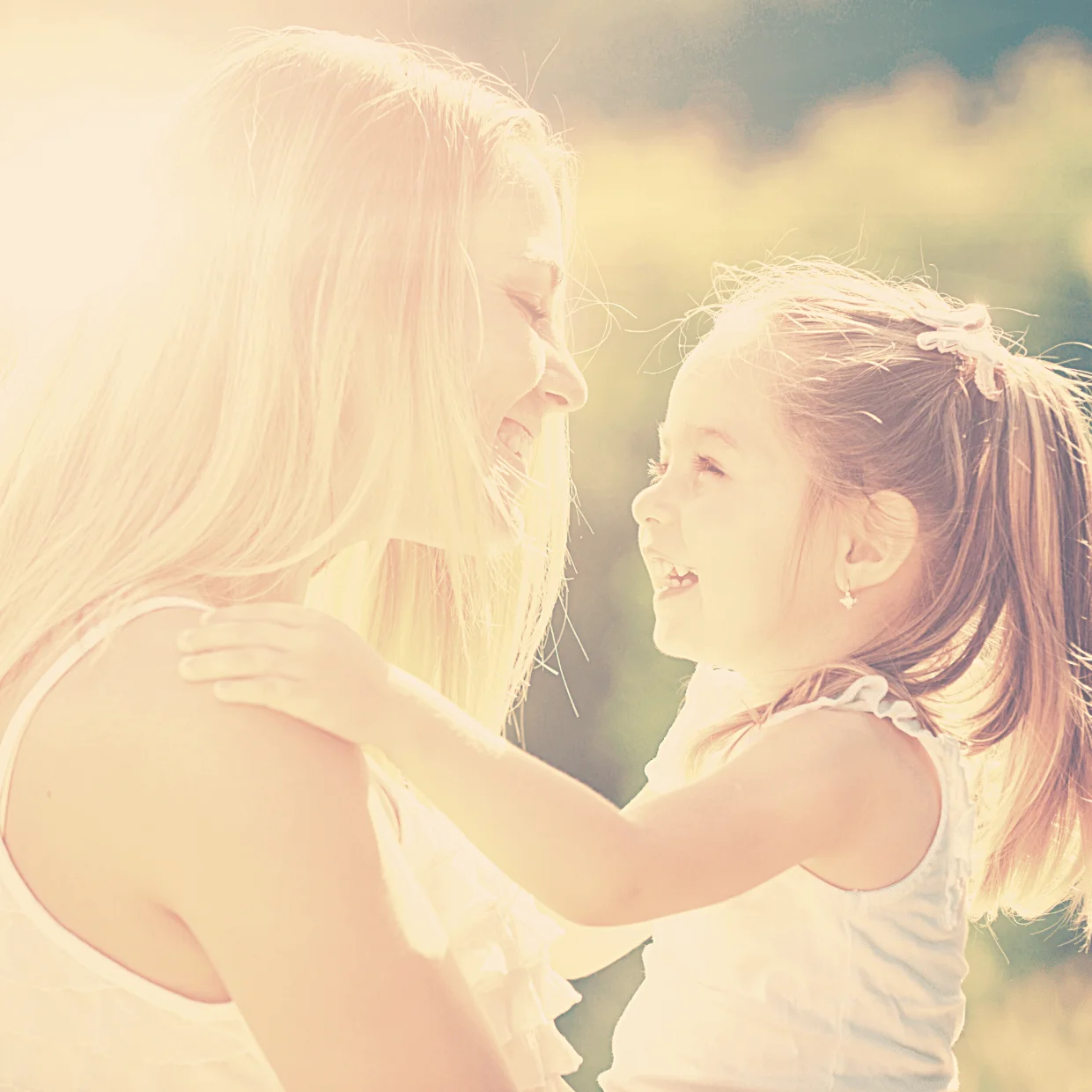 Mutter und kleine Tochter lachen sich im Sonnenlicht an