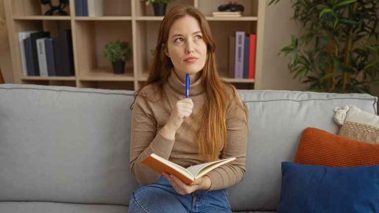 Frau sitzt mit Notizbuch und Stift auf dem Sofa und denkt nach