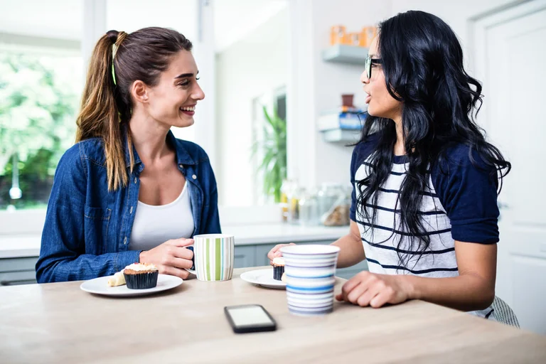 Zwei Frauen unterhalten sich lächelnd bei Kaffee am Küchentisch